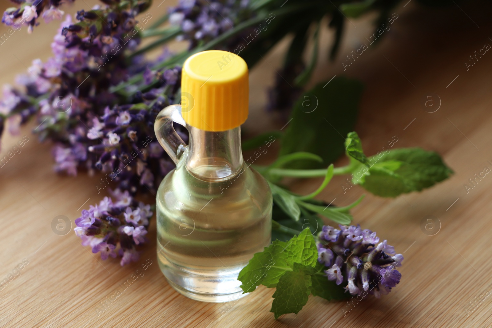 Photo of Bottle of natural essential oil, mint leaves and lavender flowers on wooden table, closeup