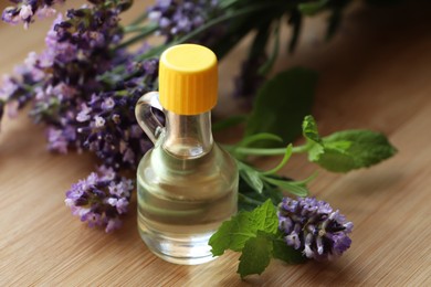 Photo of Bottle of natural essential oil, mint leaves and lavender flowers on wooden table, closeup