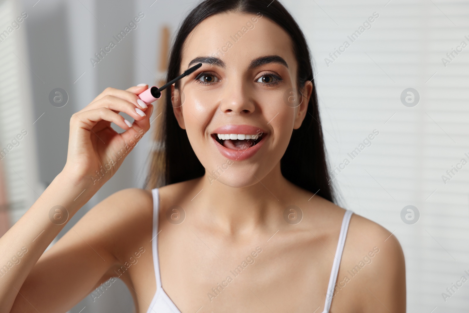 Photo of Beautiful young woman applying mascara indoors, closeup