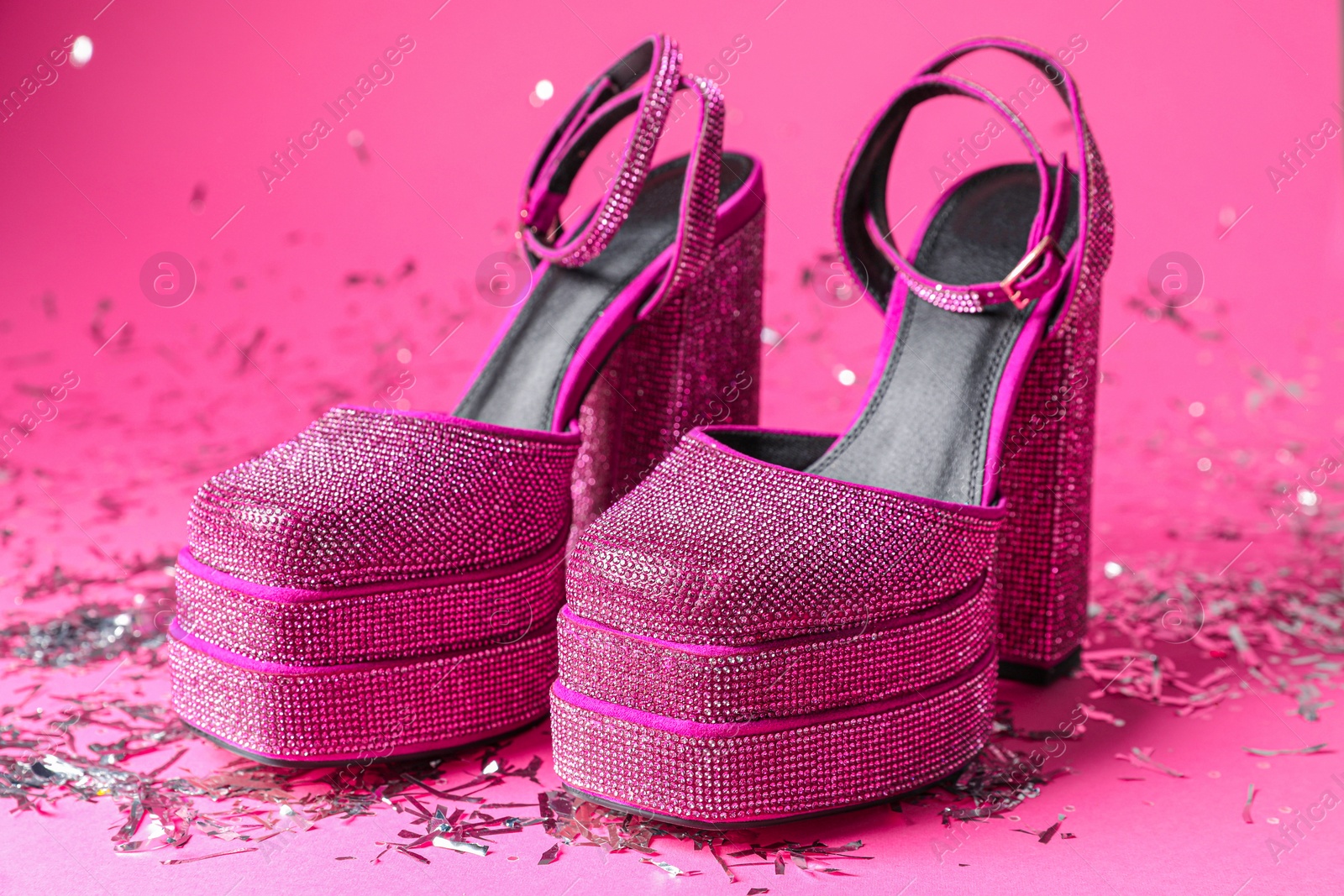 Photo of Fashionable punk square toe ankle strap pumps and confetti on pink background. Shiny party platform high heeled shoes