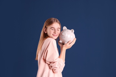 Teen girl with piggy bank on color background