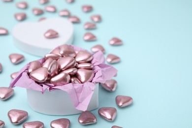 Photo of Box and delicious heart shaped candies on light blue background. Space for text