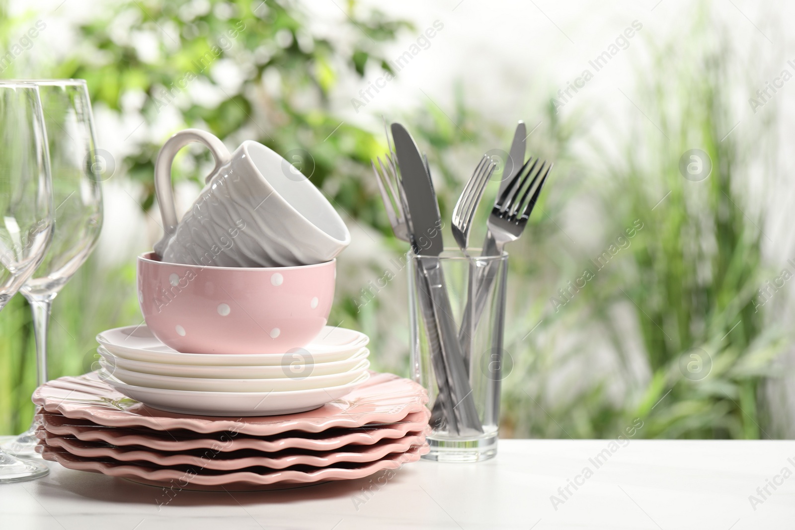 Photo of Beautiful ceramic dishware, glasses, cutlery and cup on white table outdoors, space for text