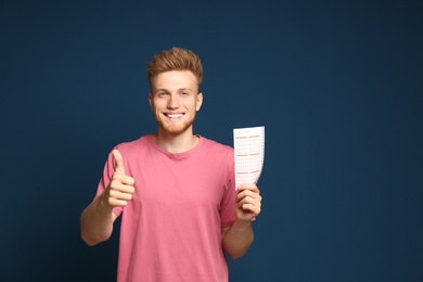 Photo of Portrait of happy young man with lottery ticket on blue background