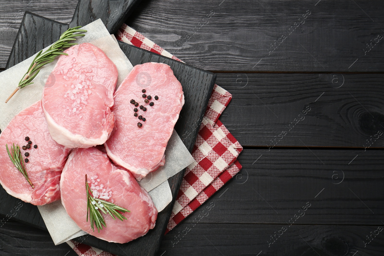 Photo of Pieces of raw pork meat and spices on black wooden table, top view. Space for text