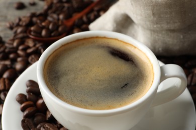Photo of Cup of hot aromatic coffee and roasted beans on table, closeup