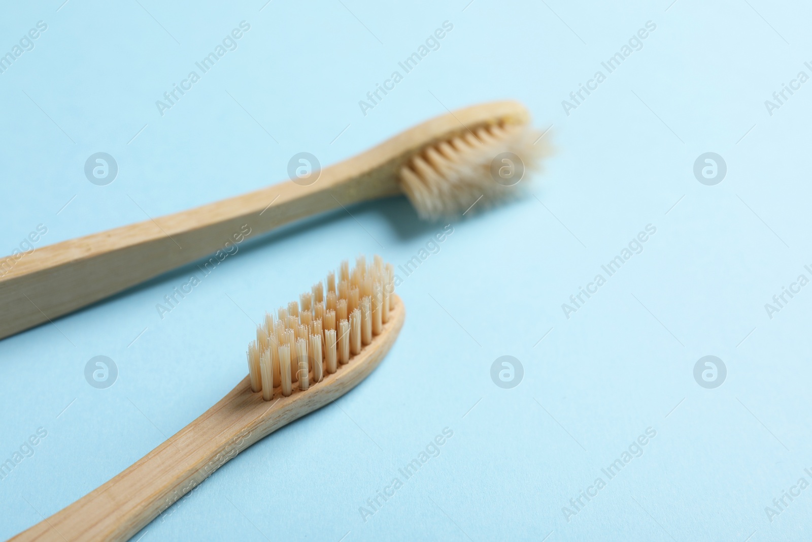 Photo of Two bamboo toothbrushes on light blue background, closeup. Space for text