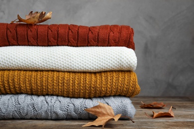 Photo of Stack of warm clothes and autumn leaves on wooden table against grey background