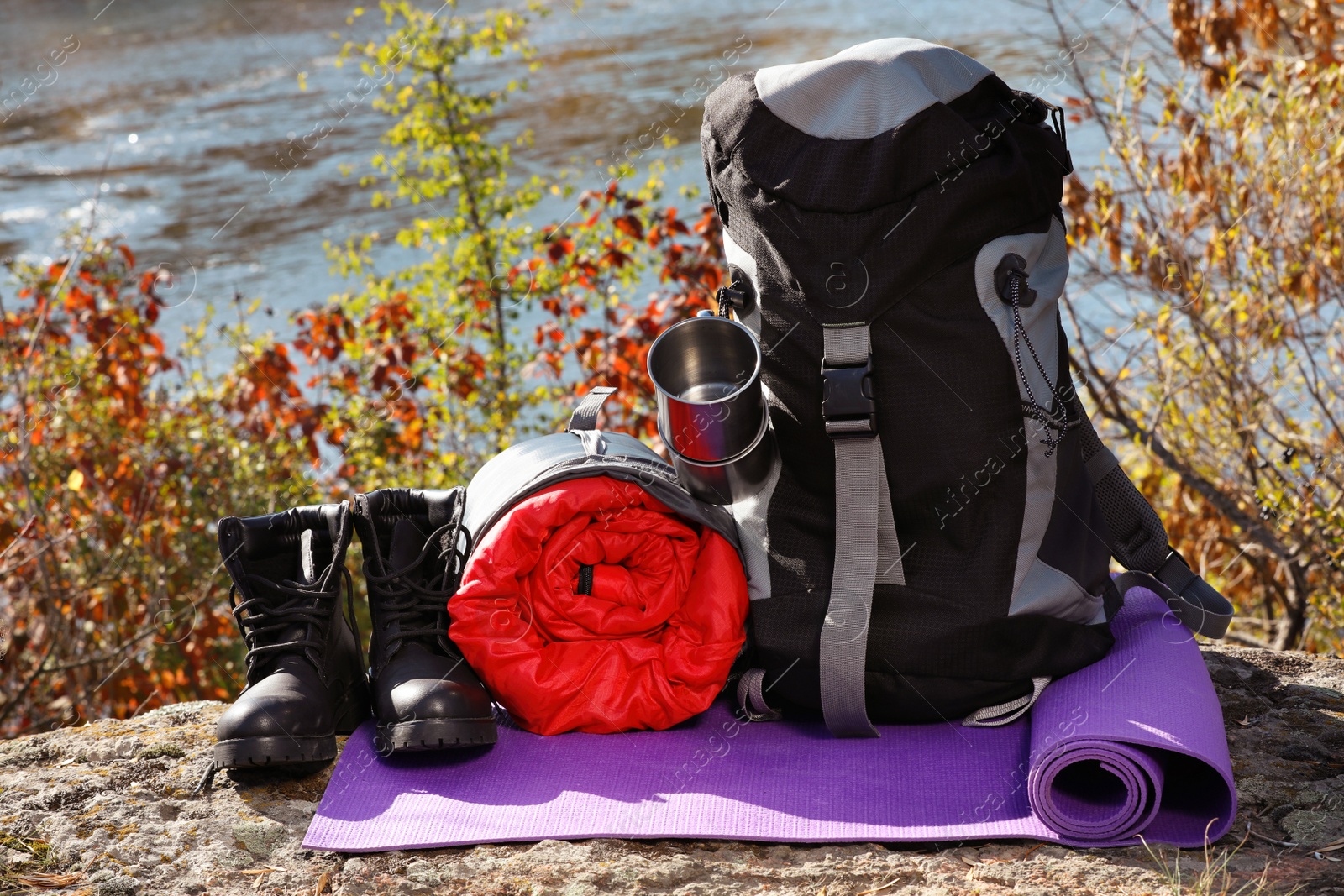 Photo of Set of camping equipment with sleeping bag on ground outdoors