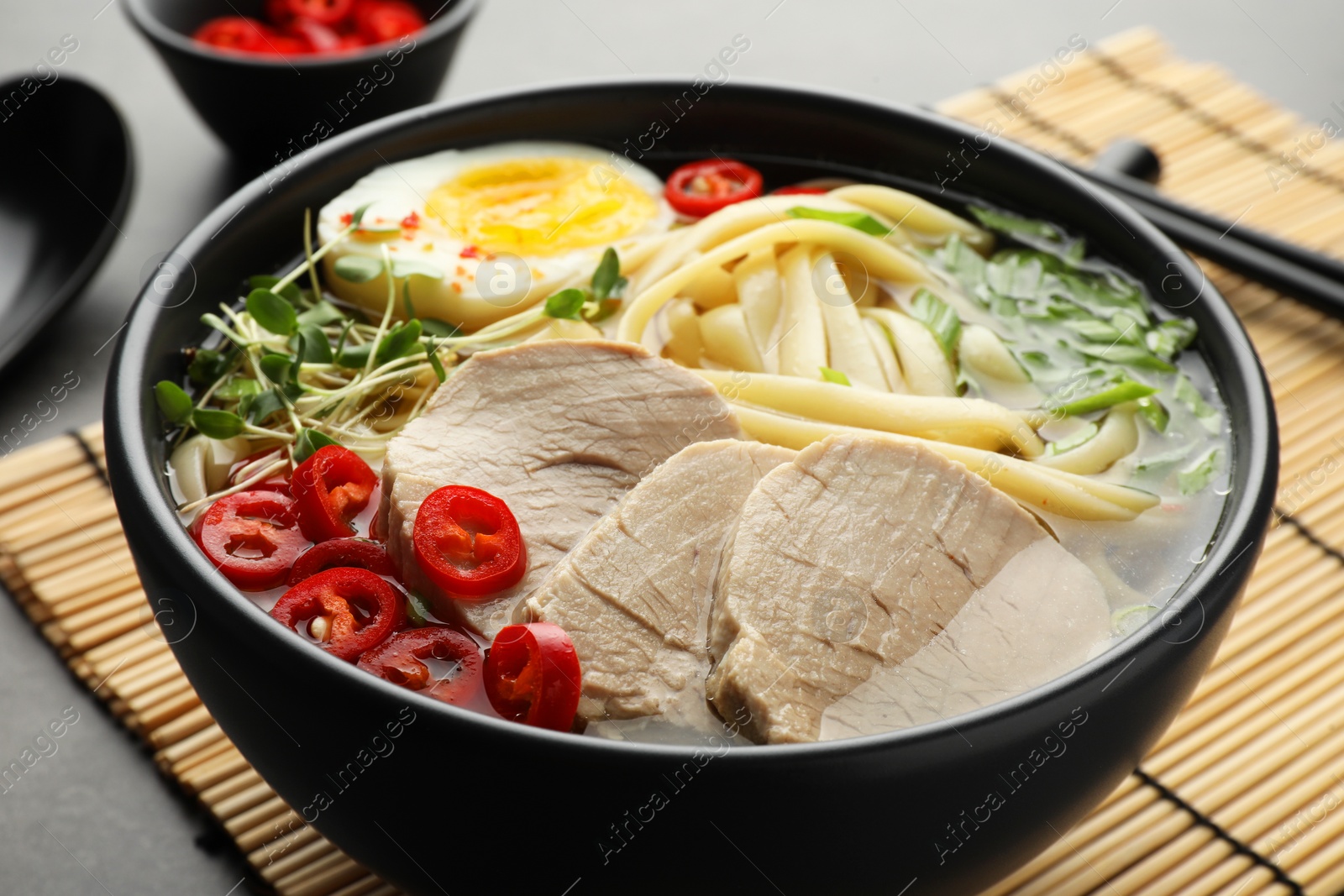 Photo of Delicious ramen with meat in bowl served on grey table, closeup. Noodle soup