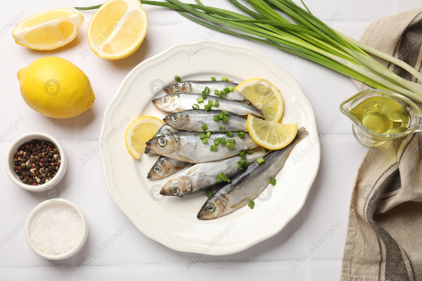 Photo of Fresh raw sprats, green onion, spices and cut lemon on white tiled table, flat lay