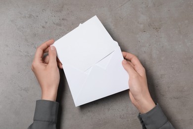 Photo of Woman taking card out of letter envelope at grey textured table, top view