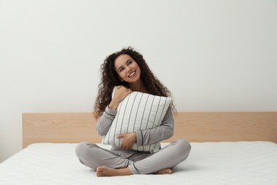 Photo of Happy young African American woman hugging pillow on bed with comfortable mattress at home
