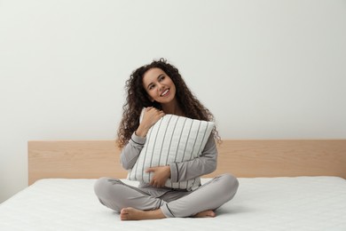 Happy young African American woman hugging pillow on bed with comfortable mattress at home