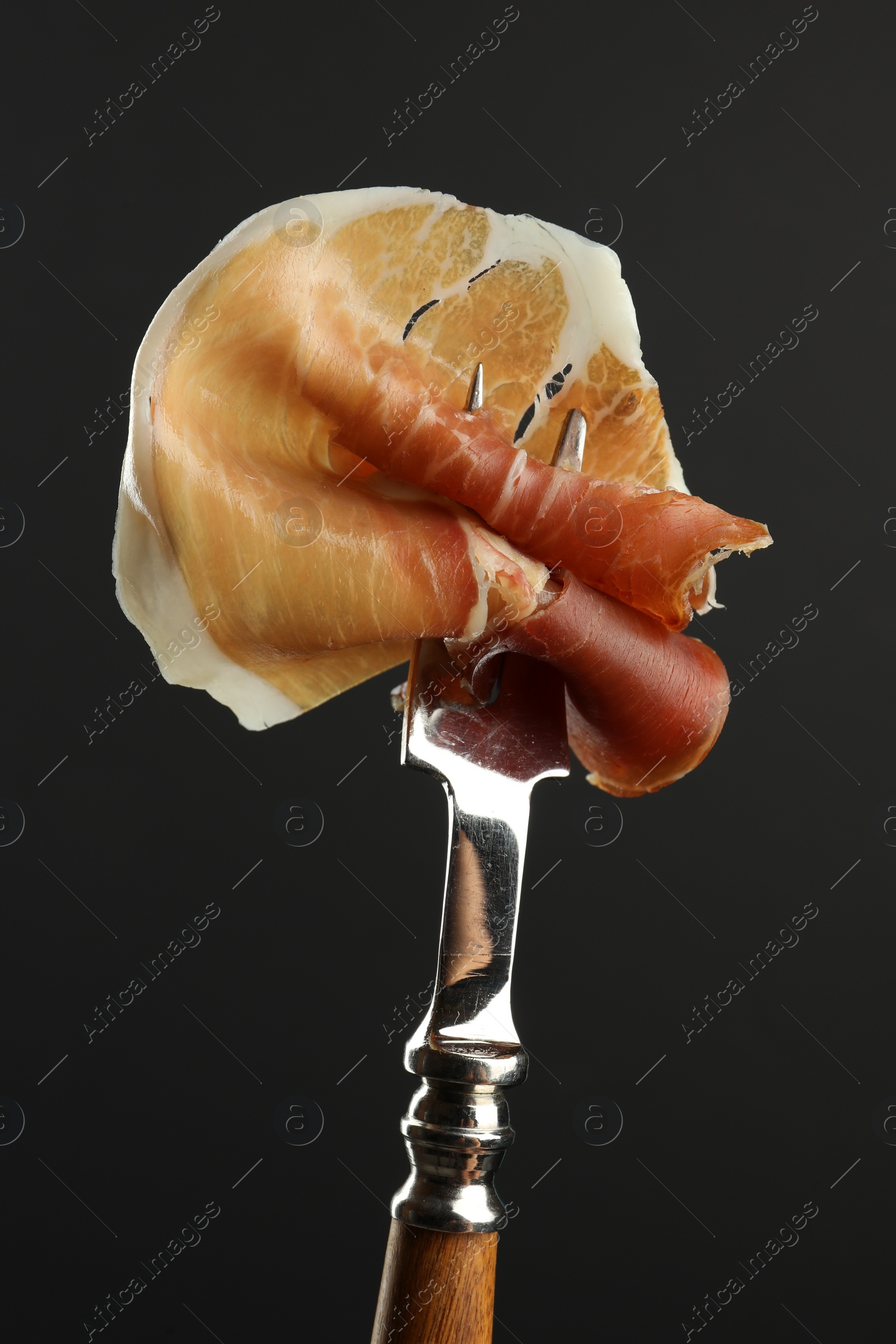 Photo of Fork with slice of tasty jamon on black background, closeup