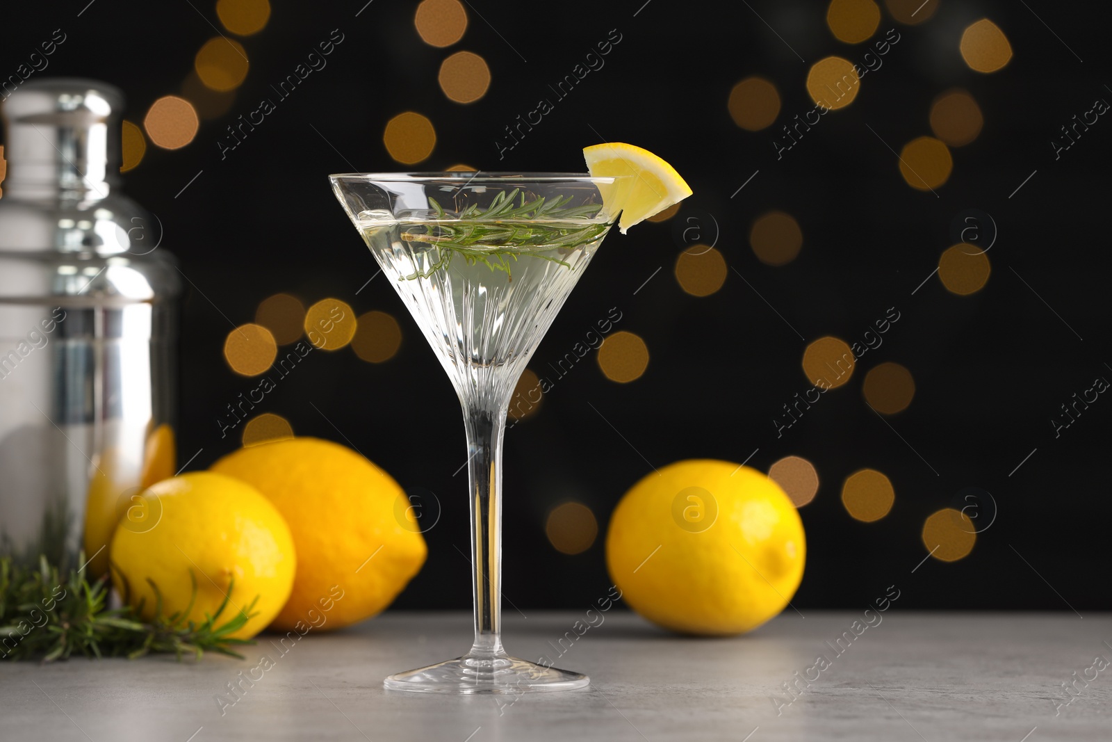 Photo of Martini glass of refreshing cocktail with lemon slice, rosemary, fruits and shaker on light grey table