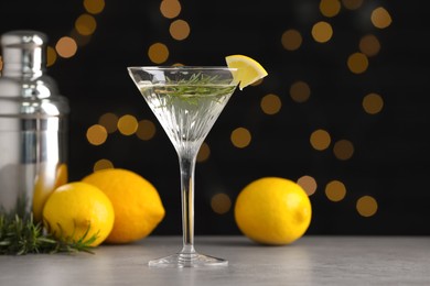 Martini glass of refreshing cocktail with lemon slice, rosemary, fruits and shaker on light grey table