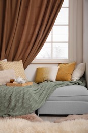 Photo of Comfortable lounge area with knitted blanket and soft pillows near window in room