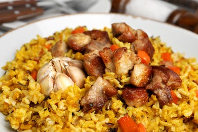 Photo of Delicious pilaf with meat, carrot and garlic on plate, closeup