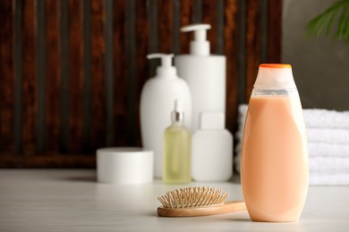 Photo of Bottle of shampoo, wooden hairbrush and toiletries on white table indoors, space for text