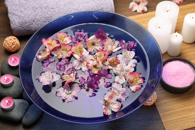 Photo of Bowl of water with flowers, candles, stones and towel on wooden table. Spa treatment