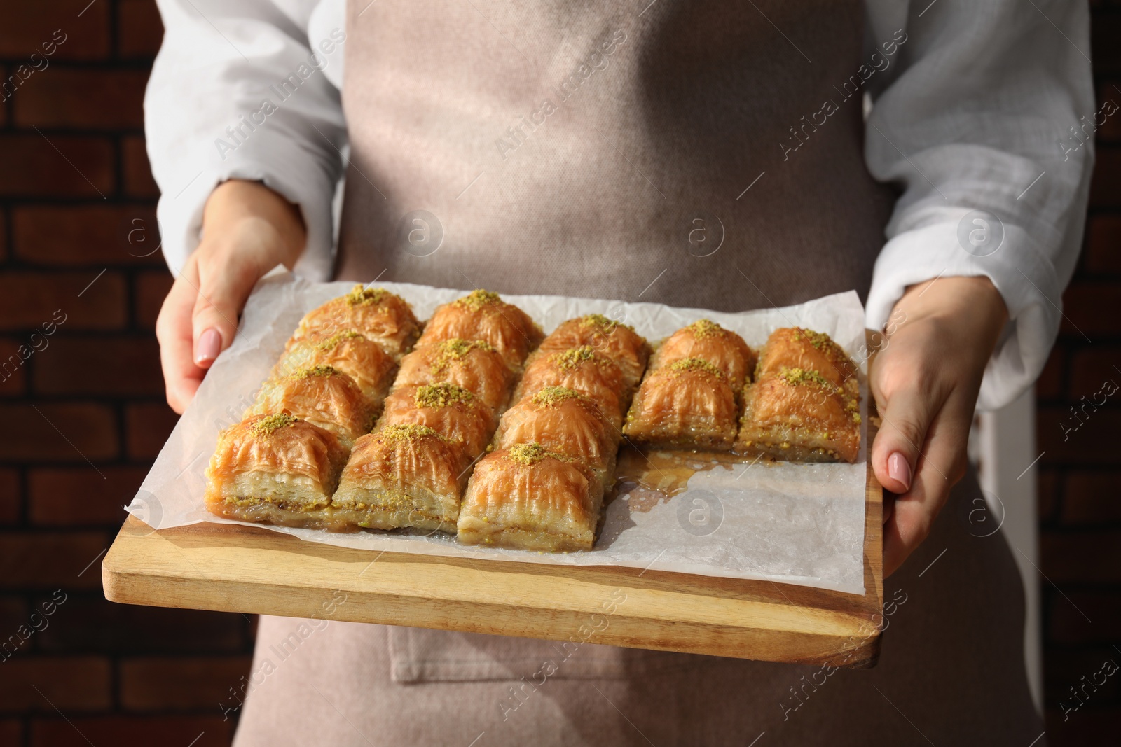 Photo of Woman with delicious sweet baklava against brick wall, closeup