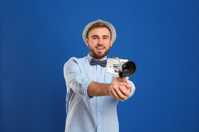 Young man with vintage video camera on blue background