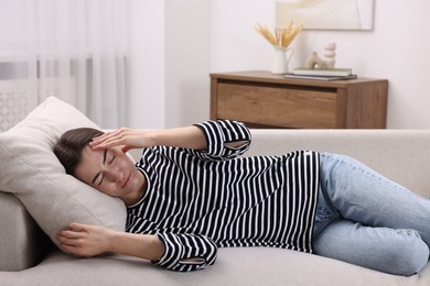 Photo of Sad woman suffering from headache on sofa indoors