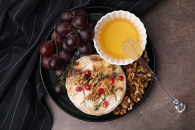 Photo of Plate with tasty baked camembert, honey, grapes, walnuts and pomegranate seeds on brown textured table, top view