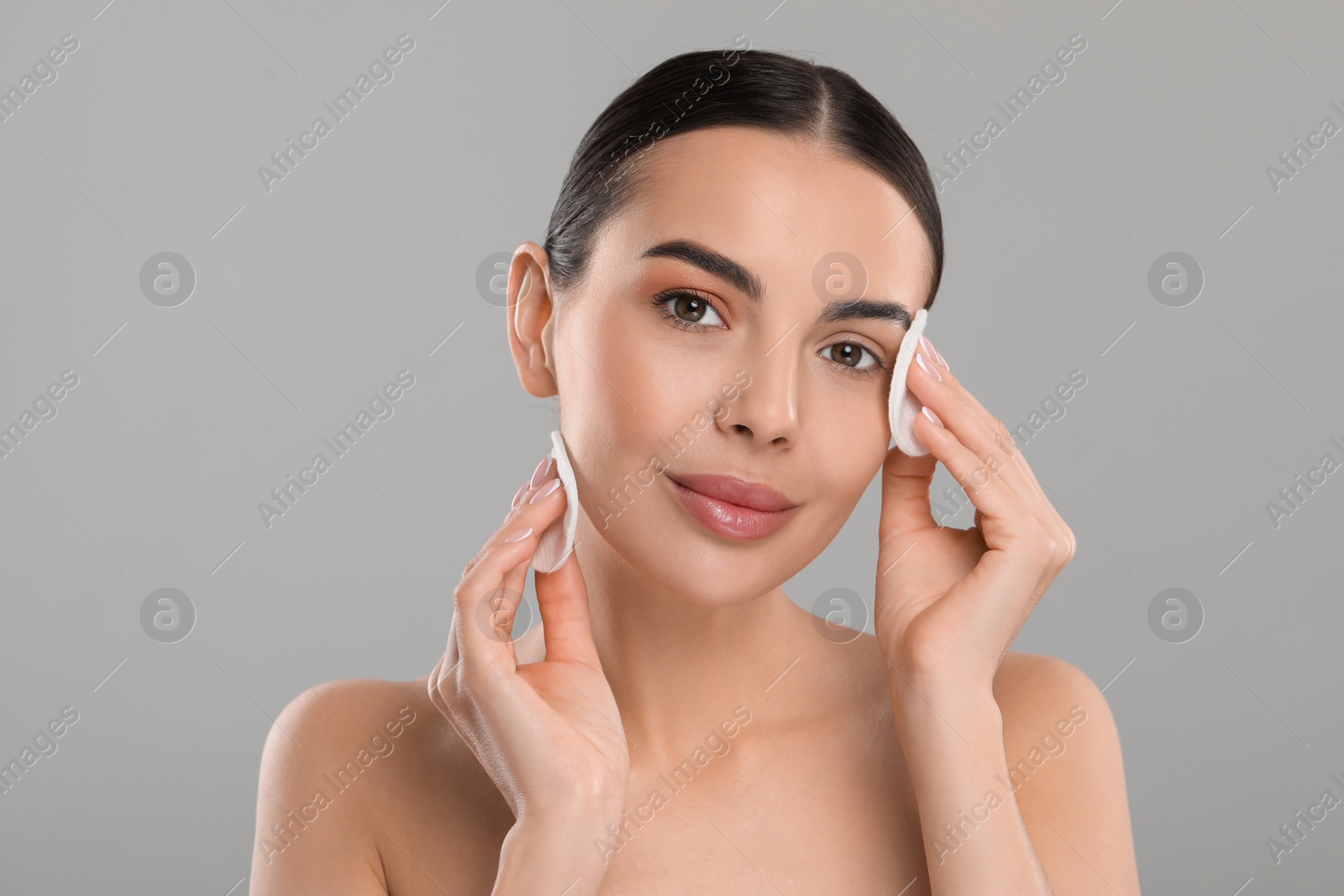 Photo of Beautiful woman removing makeup with cotton pads on light grey background