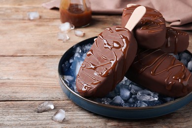 Delicious glazed ice cream bars and ice cubes on wooden table