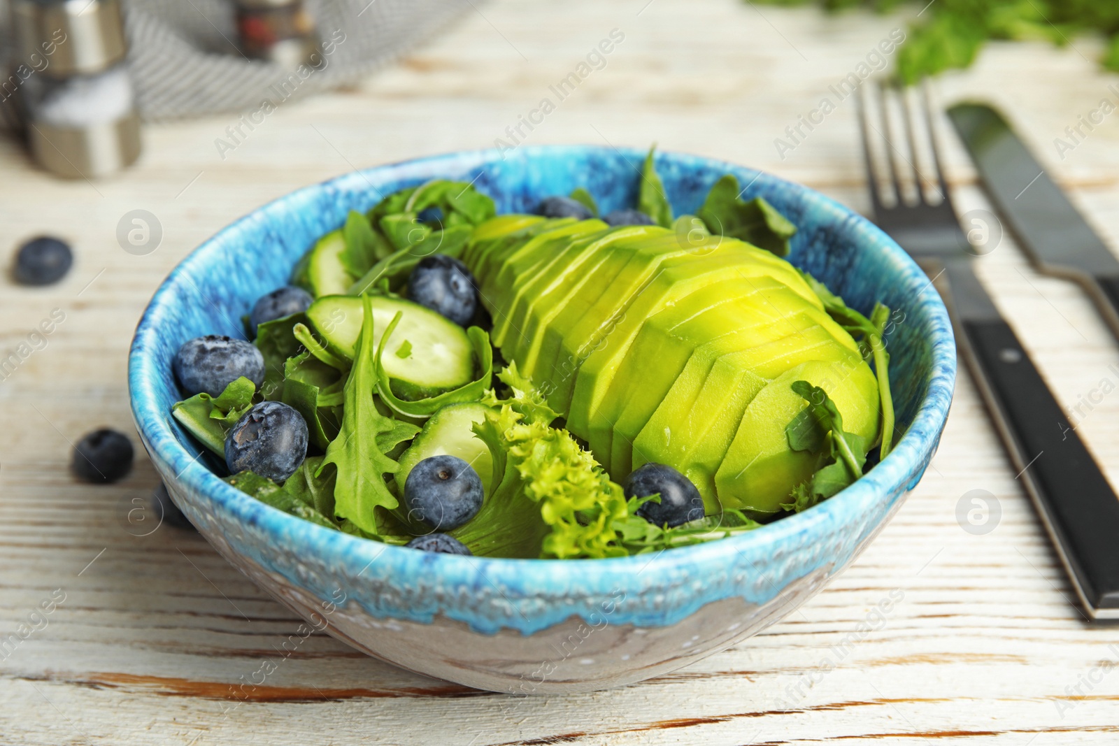 Photo of Delicious avocado salad with blueberries in bowl on white wooden table