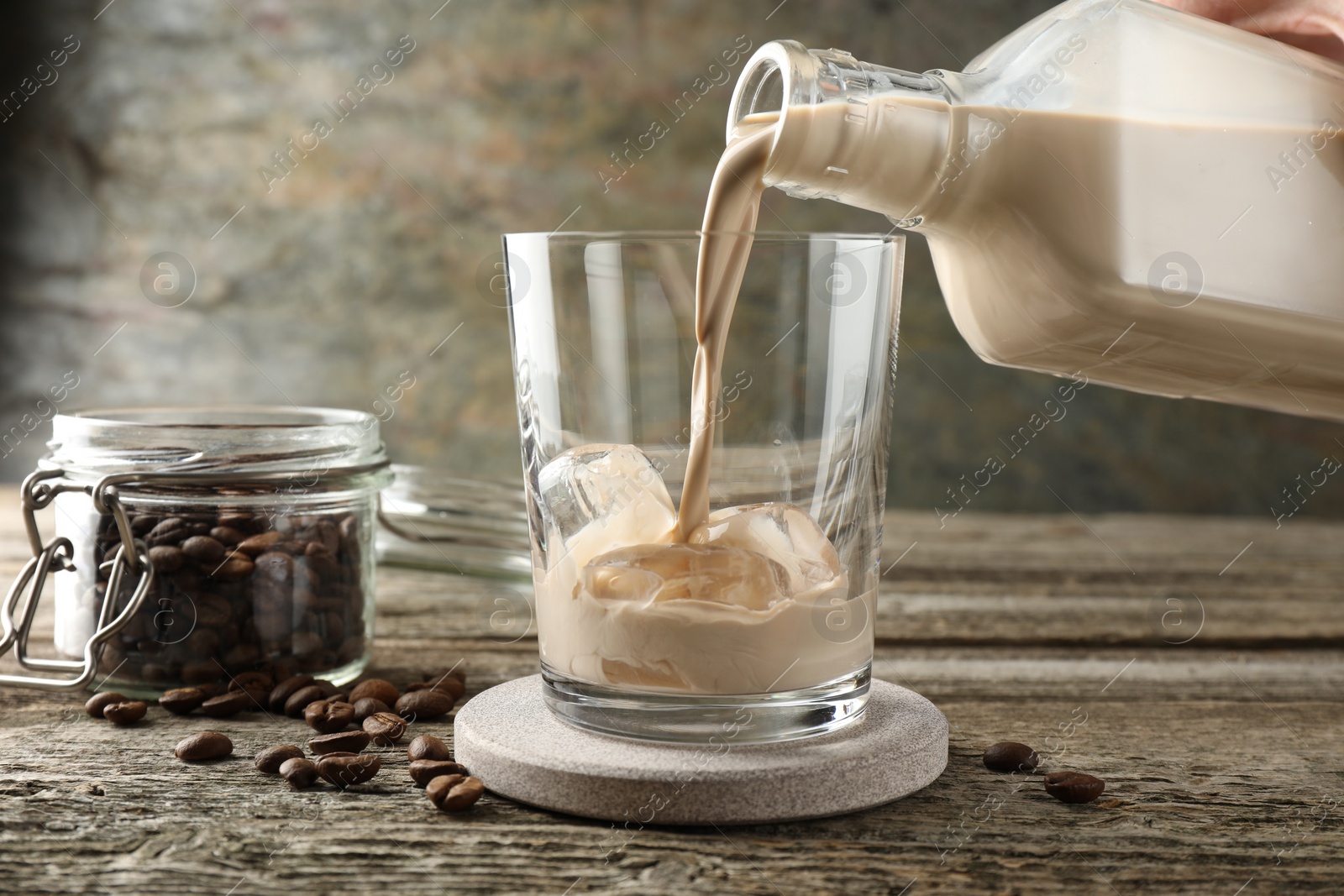 Photo of Pouring coffee cream liqueur into glass at wooden table, closeup