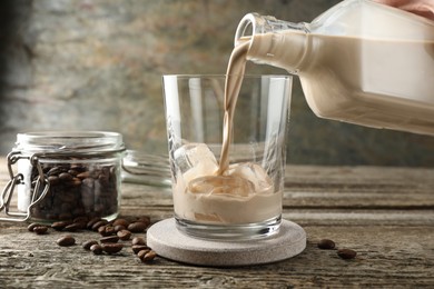 Pouring coffee cream liqueur into glass at wooden table, closeup