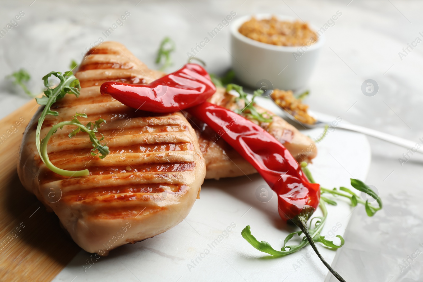 Photo of Tasty grilled chicken fillets with chili peppers and arugula on board, closeup