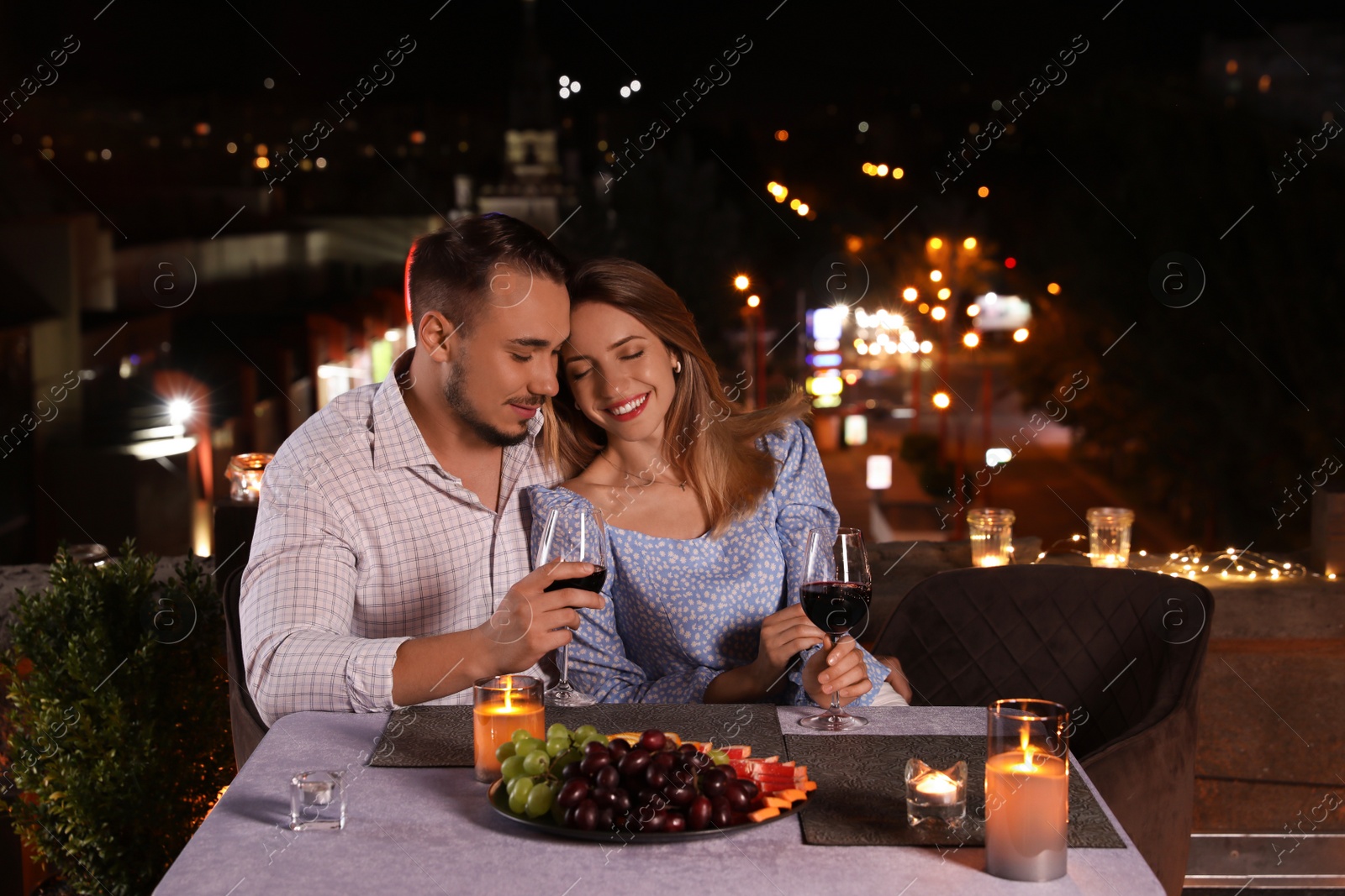Photo of Romantic couple with glasses of red wine on cafe terrace at night