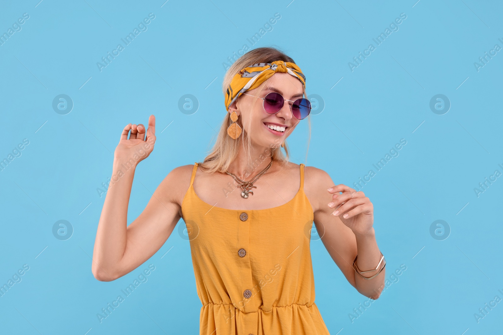 Photo of Portrait of smiling hippie woman in sunglasses dancing on light blue background