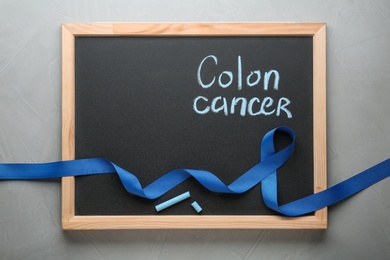 Chalkboard with blue awareness ribbon and words COLON CANCER on grey background, top view. Space for text