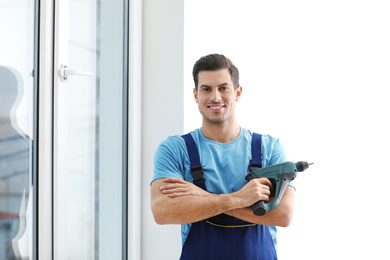 Repairman with electric screwdriver near plastic window indoors