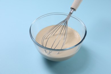 Photo of Dough and whisk in glass bowl on light blue background