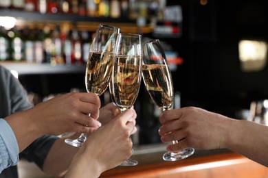 Photo of Friends clinking with glasses of champagne in bar, closeup