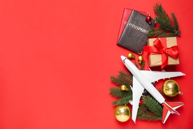 Photo of Flat lay composition with Christmas decorations, toy airplane and passports on red background, space for text. Winter vacation