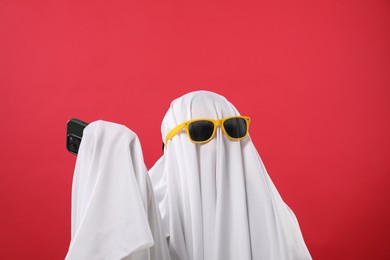 Photo of Person in ghost costume and sunglasses with smartphone on red background