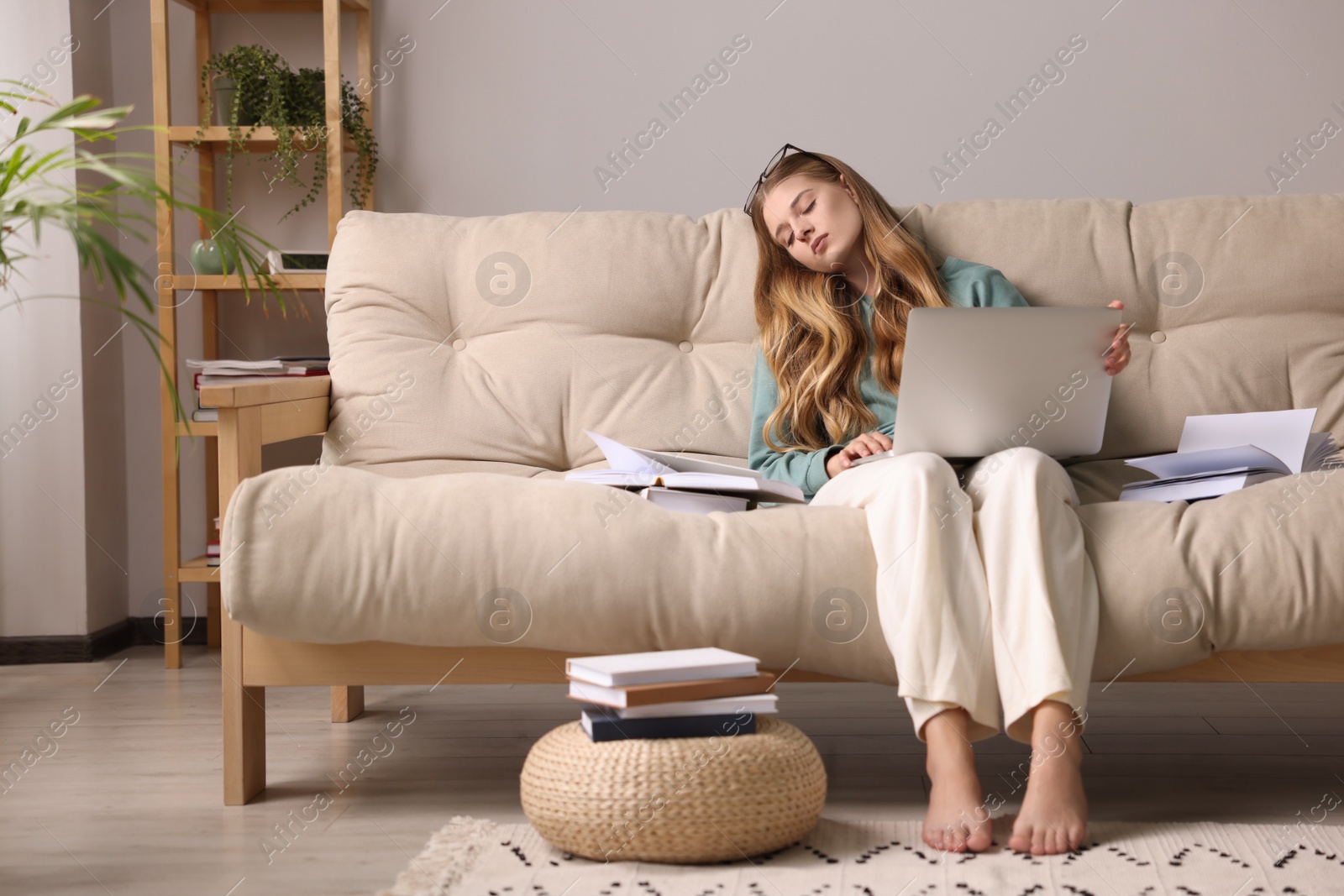 Photo of Young tired woman sleeping with laptop and books on couch at home