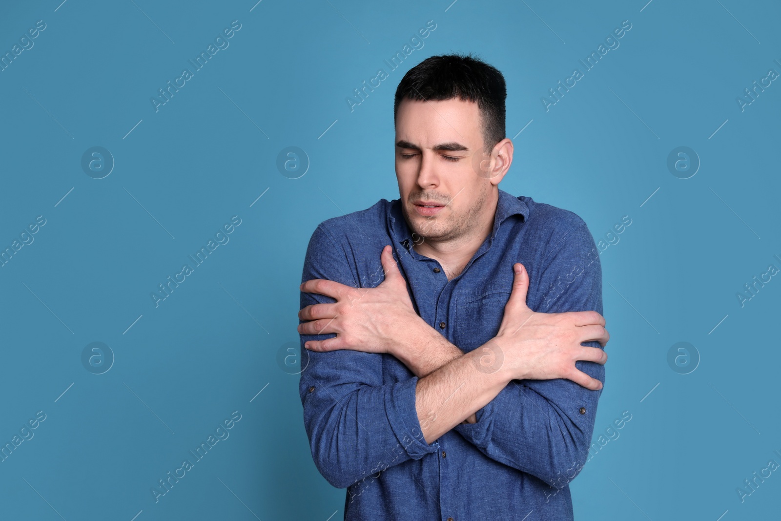 Photo of Young man suffering from fever on blue background, space for text. Cold symptoms