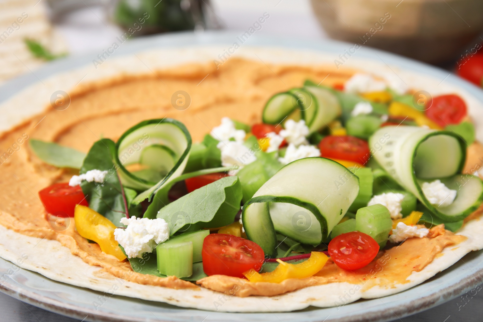 Photo of Tortilla with hummus and vegetables on table, closeup