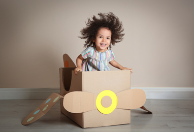Cute African American child playing with cardboard plane near beige wall