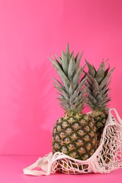 Photo of Whole ripe pineapples and net bag on pink background