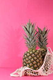 Whole ripe pineapples and net bag on pink background