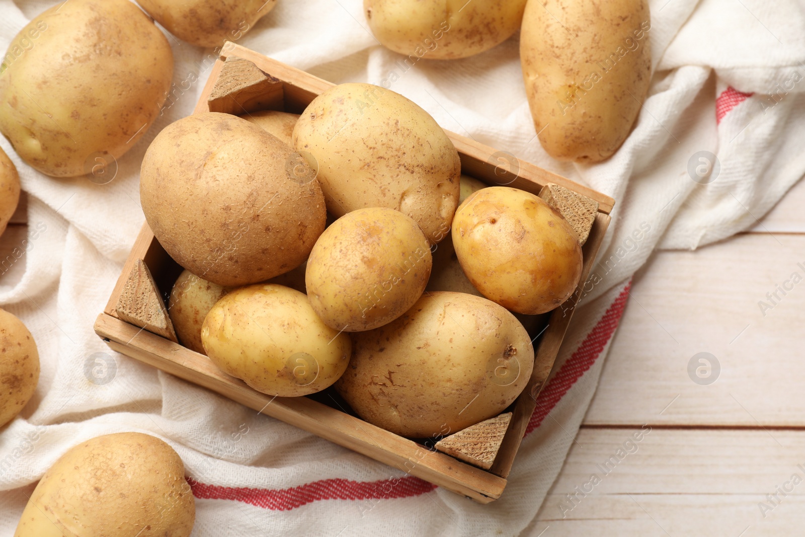 Photo of Raw fresh potatoes with crate on light wooden table, top view